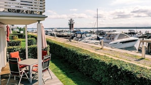 Ein Yachthafen mit vertäuten Booten, ein Leuchtturm im Hintergrund und eine Terrasse mit Sitzmöbeln.