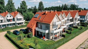 Ein Wohnkomplex mit mehreren Häusern, jeweils mit roten Ziegeldächern, Balkonen und einem gepflegten Rasen.