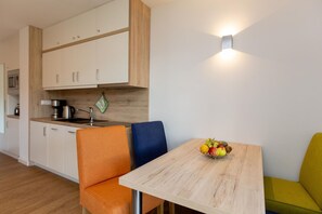 Une cuisine moderne avec des meubles blancs, un plan de travail en bois et un panier de fruits posé sur une table.