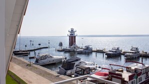 A marina with several boats docked, a lighthouse in the background, and a clear view of the water.