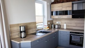 A modern kitchen with grey cabinetry, a wooden countertop, a coffee maker, a kettle, a toaster, and a built-in oven.