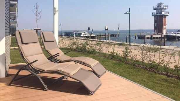 A wooden deck with two lounge chairs facing a marina with boats and a lighthouse. - Corner apartment with 2 terraces with parking at the house, dog allowed P7 A5 - 2 (Plau am See)
