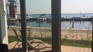 A view from a room with a wooden deck overlooking a marina with boats and a lighthouse. - Corner apartment with 2 terraces with parking at the house, dog allowed P7 A5 - 2 (Plau am See)