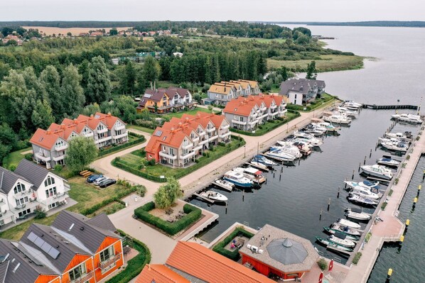 A marina with boats docked, surrounded by residential buildings with red roofs and a view of a lake.