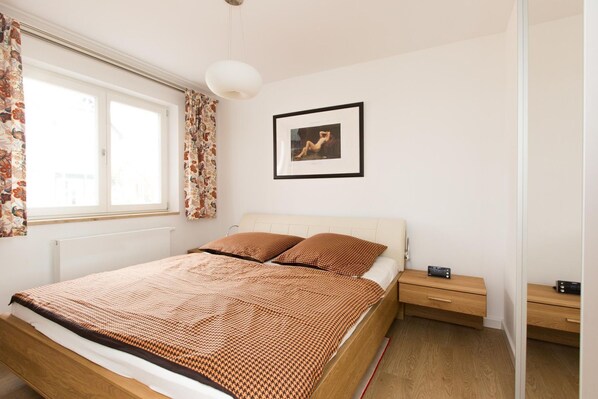 A neatly arranged bedroom with a bed, bedside tables, a framed picture on the wall, and a window with curtains.