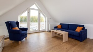 Une chambre de style loft moderne, avec un plafond en pente, une grande fenêtre, un canapé bleu, un fauteuil bleu et une table basse en bois.