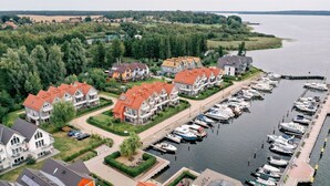 Un port de plaisance où sont amarrés des bateaux, entouré d’immeubles résidentiels aux toits rouges, avec vue sur un lac.