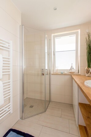 Une salle de bain moderne avec une douche à l’italienne en verre, un sol carrelé de blanc, un plan de travail en bois et une fenêtre offrant une belle vue.