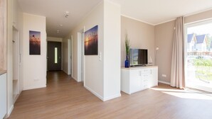 Un pasillo moderno con suelo de madera, una consola blanca con un televisor de pantalla plana y obras de arte en las paredes.