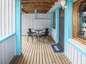 Un espace extérieur abrité, doté d’une terrasse en bois, de chaises en métal et d’une petite table.