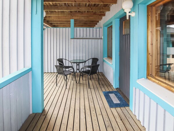 A covered outdoor seating area with a wooden deck, metal chairs, and a small table.