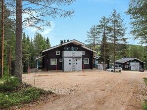 Une cabane à deux étages, avec une allée en gravier, entourée de grands pins.
