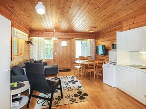 L’intérieur chaleureux d’un chalet comprend un canapé, une table à manger, des chaises, un coin cuisine et un téléviseur.