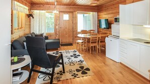A cozy cabin interior with a wooden ceiling, a dining area with a table and chairs, a sofa, a kitchen with white cabinets, and a television. - Taukotuli 4 paritalon alakerta by Interhome (Hyrynsalmi)