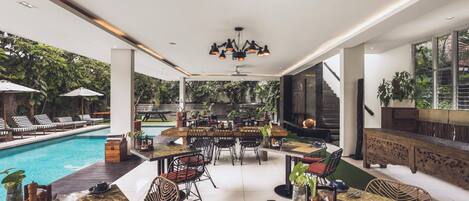 Un espace piscine intérieur agrémenté de chaises longues, de tables et de chaises, le tout entouré de verdure.