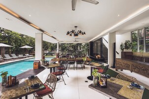 Un área de piscina interior con sillones, mesas y sillas, rodeada de vegetación.