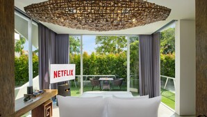 A modern room with a large window, a Netflix sign, a sofa, and a dining area with a table and chairs. - Monolocale Resort & Spa Seminyak by Ini Vie Hospitality (Keroboken Kelod)