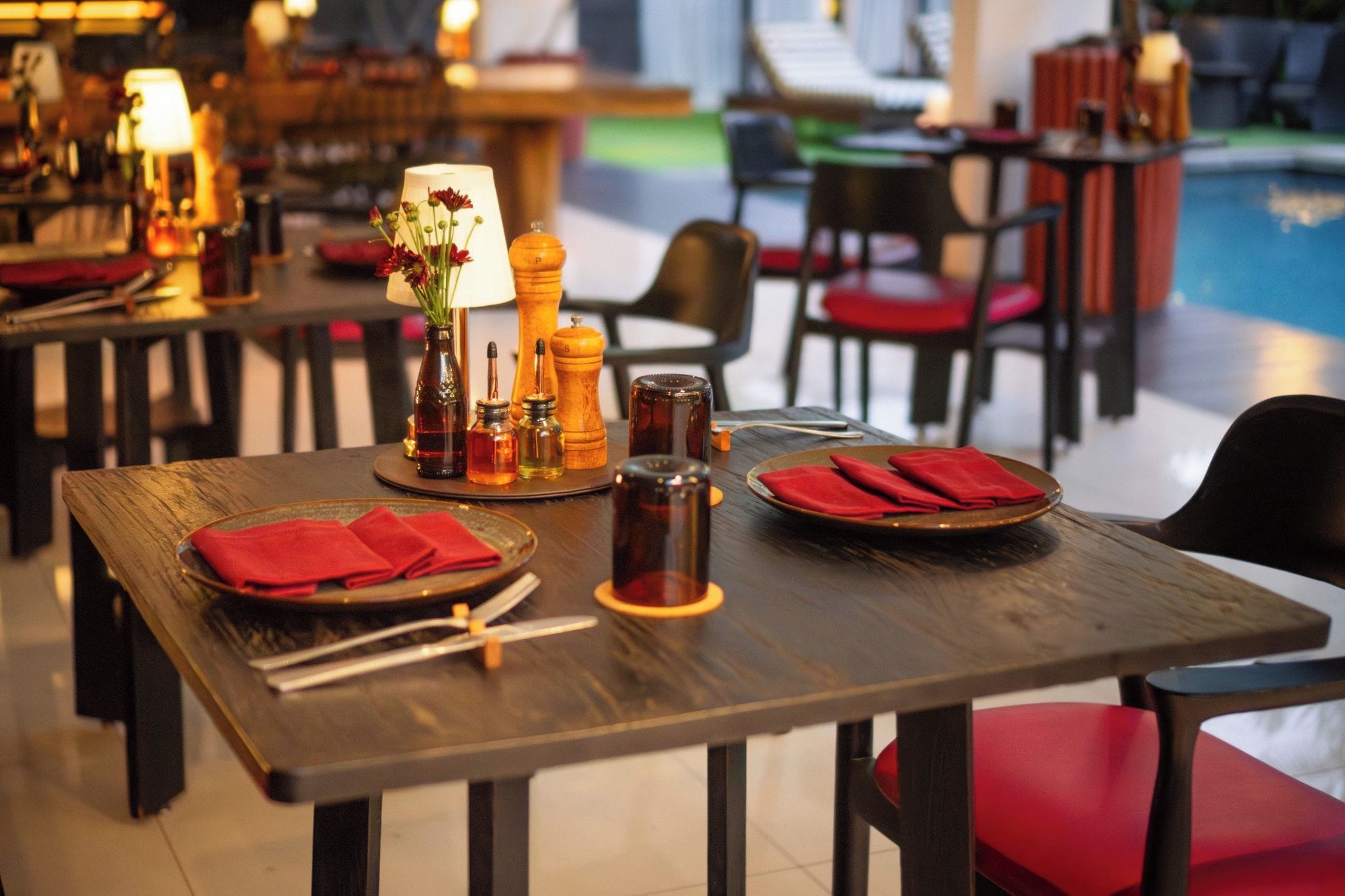 Un'ambientazione di ristorante con tavoli apparecchiati per la cena, comprensivi di piatti, posate e condimenti.