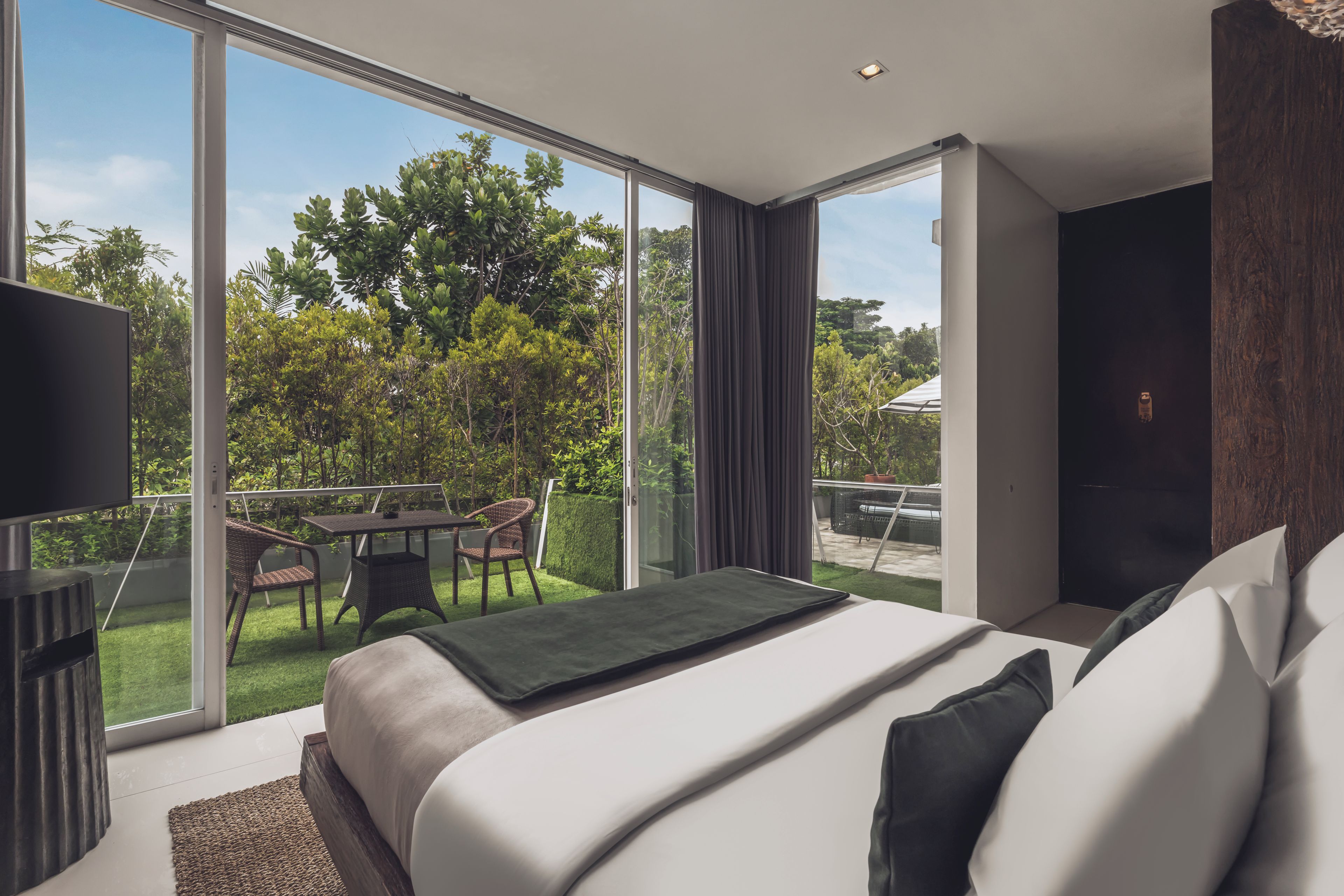 Ein modernes Hotelzimmer mit einem großen Bett, einem Flachbildfernseher und einem Balkon mit Tisch und Stühlen.