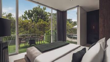 A modern hotel room with a large bed, a flat-screen TV, a balcony with a table and chairs, and a view of greenery.