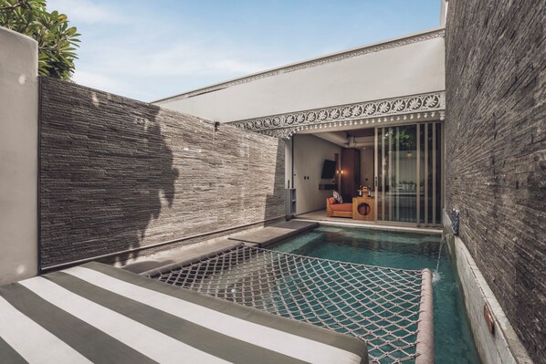 A modern outdoor pool area with a stone wall, a seating area with cushions, and a glass door leading to a room. - Monolocale Resort & Spa Seminyak by Ini Vie Hospitality (Keroboken Kelod)
