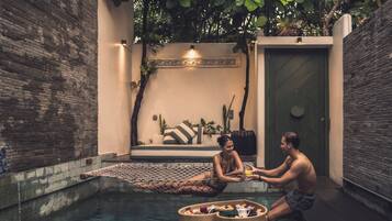 Una pareja descansando junto a una piscina con una hamaca y cestas de frutas y flores.