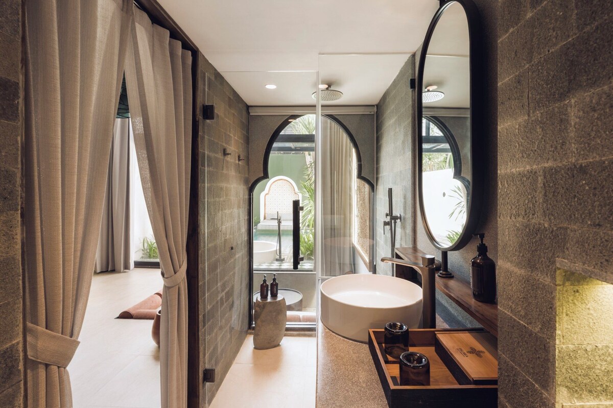 A modern bathroom with a large bathtub, a round mirror, and a view of a pool.
