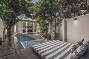 A modern outdoor pool area with a lounge chair and a bed with striped bedding. - Monolocale Resort & Spa Seminyak by Ini Vie Hospitality (Keroboken Kelod)