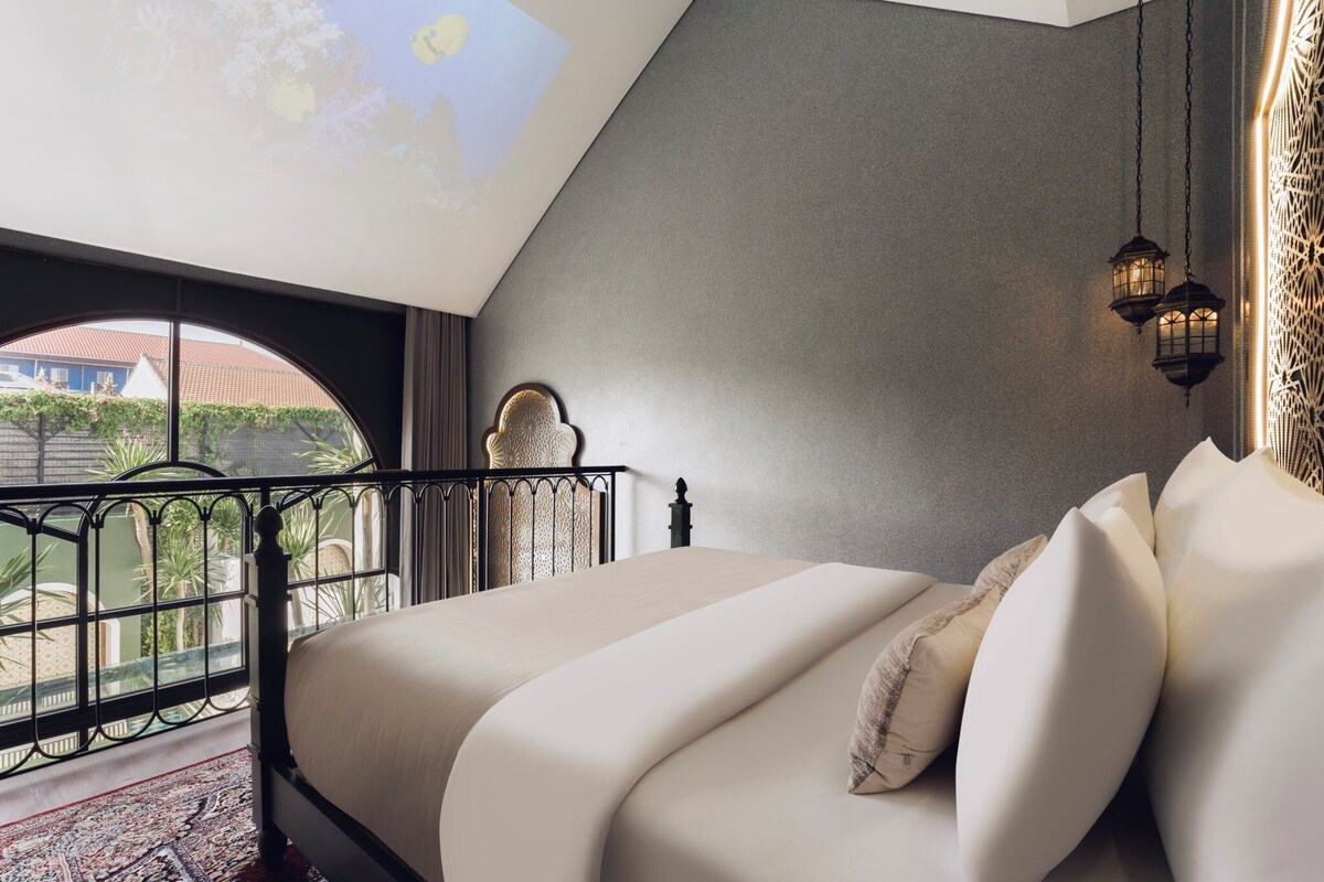A bedroom with a bed, a view through a window, and a decorative wall.