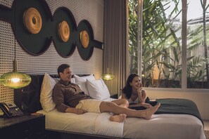 A bedroom with a bed, two bedside lamps, a nightstand with a phone, and a window with a view of greenery. - Monolocale Resort & Spa Seminyak by Ini Vie Hospitality (Keroboken Kelod)