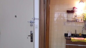 Una habitación con una puerta cerrada, un armario de madera, un muro con azulejos y un pequeño cubo de basura.