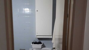 Un baño pequeño y estrecho con un inodoro, un armario blanco sobre el inodoro y un cubo de basura blanco a la izquierda.