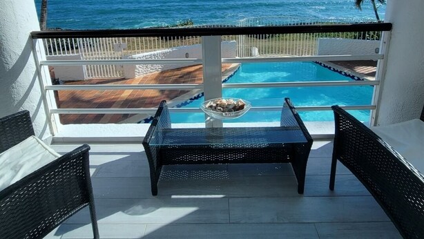 Un balcon avec vue sur l’océan, une piscine et deux fauteuils en osier.