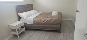 A neatly made bed with white and brown bedding, a small bedside table with a drawer, and a patterned wall.