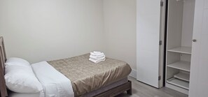 A bedroom with a bed, a bedside table, a wardrobe, and a stack of towels.
