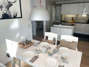 Ruokailutila, jossa on neljälle katettu ruokapöytä, valkoiset tuolit ja riippuvalaisin.
