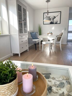 A modern kitchen with white cabinetry, a dining area with white chairs, and a pendant light above the table. - Sea breeze DUE/08 - dune bottom (Sylt)