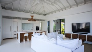 Un espacio habitable moderno con un sofá blanco grande, una cocina con muebles blancos, una zona de comedor y un televisor de pantalla plana montado en la pared.