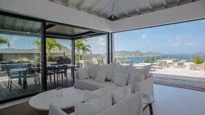 Un espacio exterior moderno con un sofá blanco, mesa de comedor y sillas, con vistas a un paisaje marino.