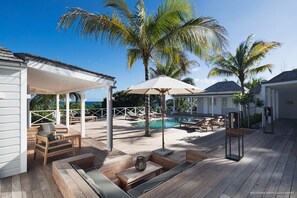 Een houten terras met loungebedden, een zwembad en parasols.