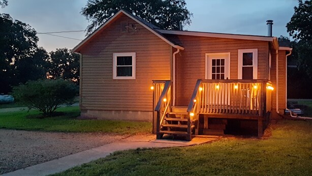 Una casa de madera con porche, escalones e iluminacion tipo guirnalda.