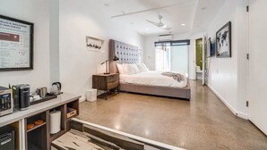 A modern hotel room with a large bed, a desk with a coffee maker, and a view of the city.