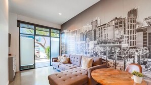 A modern living room with a large sectional sofa, a round wooden coffee table, and a cityscape mural on the wall.