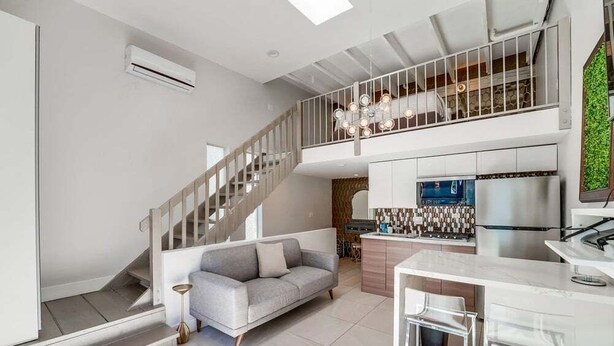 Eine moderne Küche mit Backofen, ein Essbereich mit weißem Tisch und Stühlen sowie ein graues Sofa.