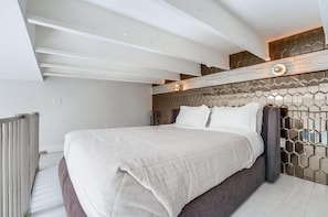 A modern bedroom with a large bed, a wooden headboard with a geometric pattern, and a white ceiling with exposed beams. - Bright & Modern 2 Level Unit in heart of Little Italy (San Diego)