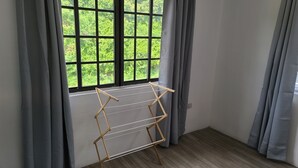 Quarto com janela, cortinas cinzas e um varal de madeira.