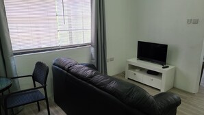 Uma sala de estar com um sofá de couro preto, uma mesinha e uma televisão sobre um suporte branco.