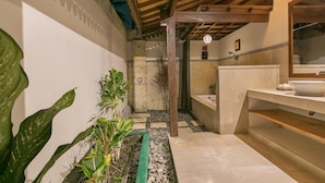 A modern bathroom with a stone shower, a sink with a mirror, and a green planter with plants. - Frida Villa Ubud by Best Deals Asia Hospitality (Ubud)