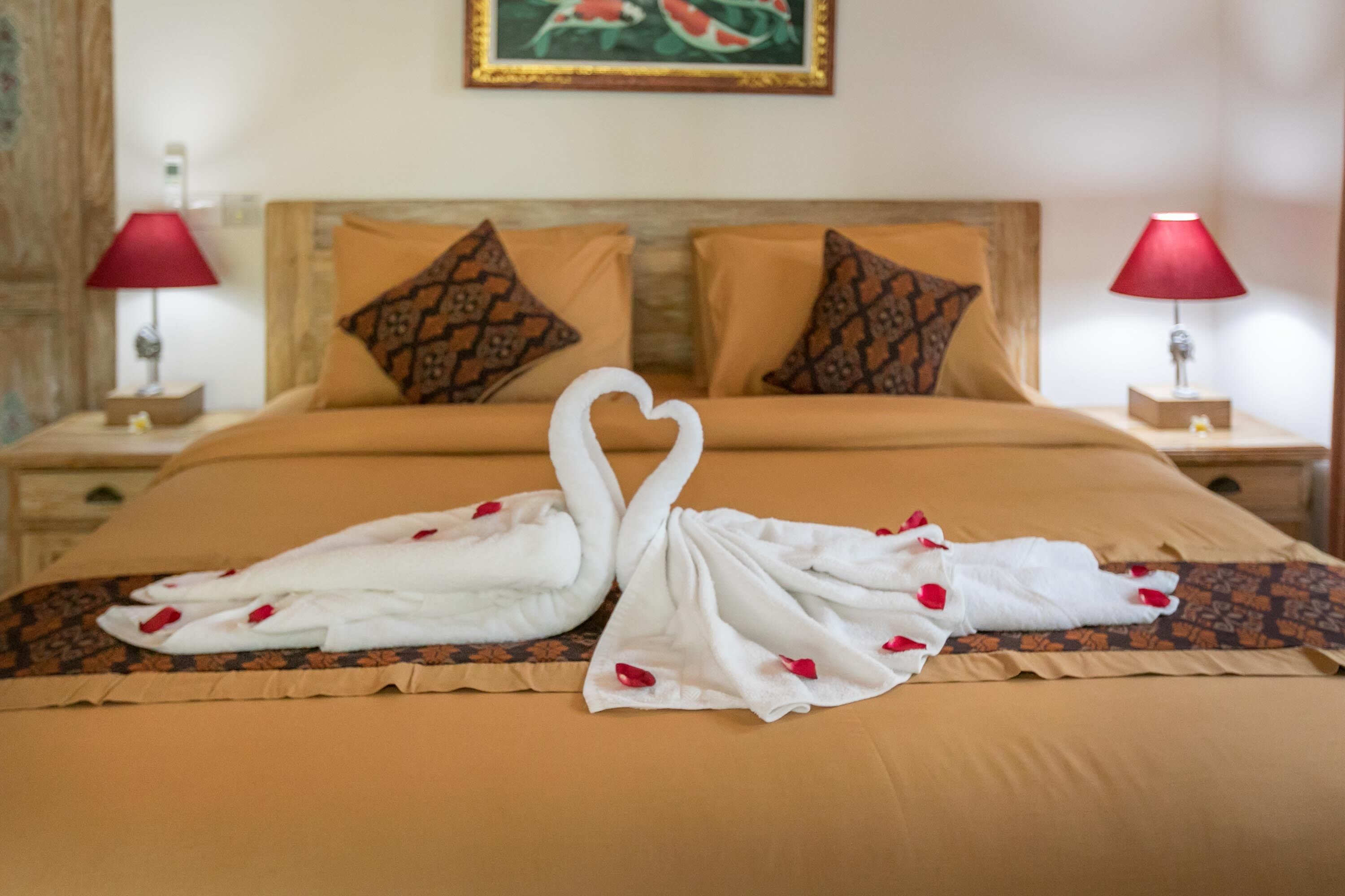 A bed with a heart-shaped towel arrangement and rose petals.