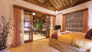 A spacious bedroom with a large bed, wooden ceiling beams, a dining area, and a view through a glass door. - Frida Villa Ubud by Best Deals Asia Hospitality (Ubud)